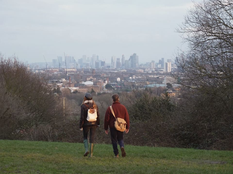 Two people walking on Parliament Hill, with the towers of the City of London on the skyline.